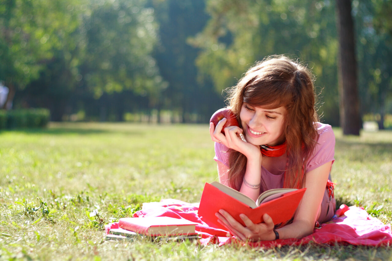 the,happy,woman,lays,on,a,grass,and,reads,the